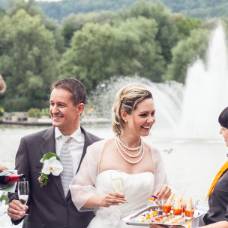 Ein Brautpaar mit zwei Servicekräften. Im Hintergrund sieht man das Hochzeitsapéro und einen Springbrunnen im Wasser.