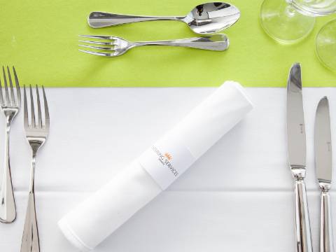 Besteck, drei Weingläser und eine Serviette mit dem Logo von Catering Services auf einer Tischdecke