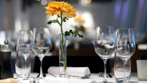 Weingläser, Trinkgläser, Besteck, weisse Servietten sowie eine Blume und Kerze auf einem Tisch mit weisser Tischdecke