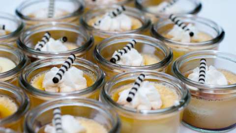 Mehrere kleine Sturzgläser gefüllt mit Dessert, das mit Sahne und einem Schokoladenröllchen dekoriert ist