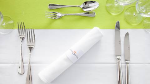 Besteck, drei Weingläser und eine Serviette mit dem Logo von Catering Services auf einer Tischdecke